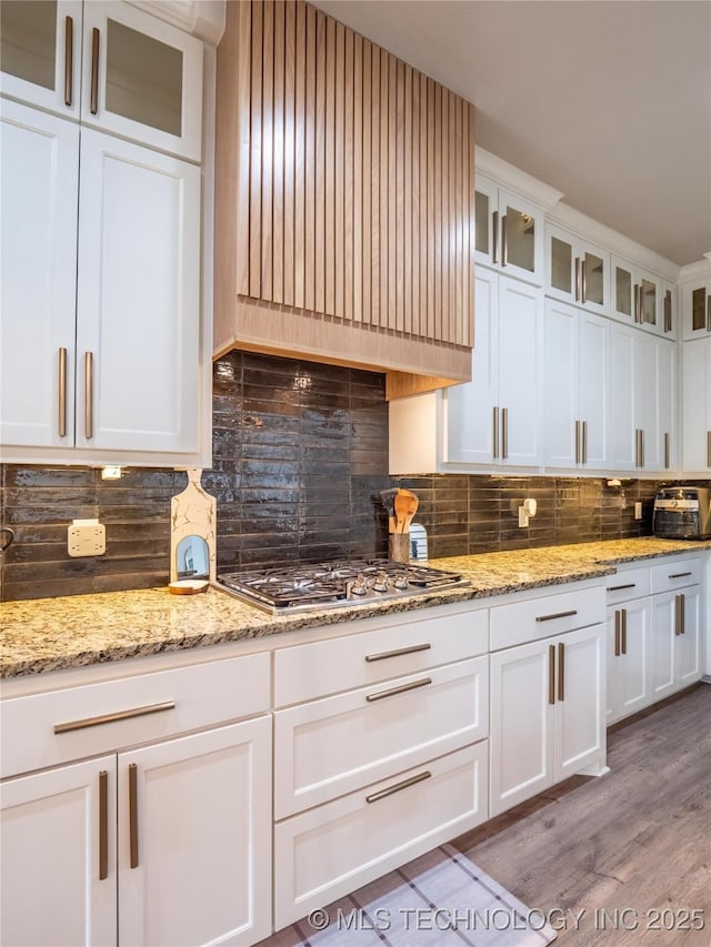 kitchen with white cabinets, hardwood / wood-style floors, backsplash, and stainless steel gas stovetop