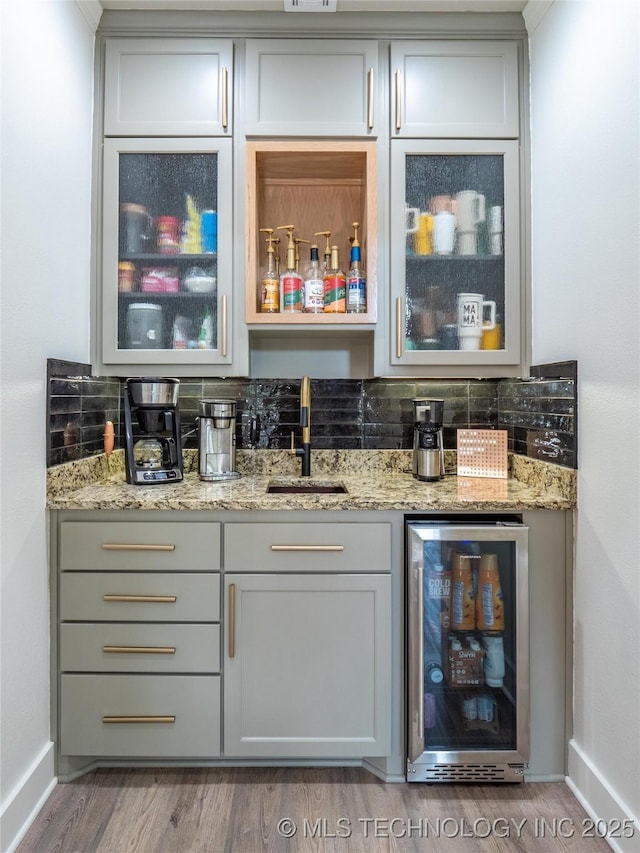 bar featuring hardwood / wood-style floors, light stone countertops, sink, and beverage cooler