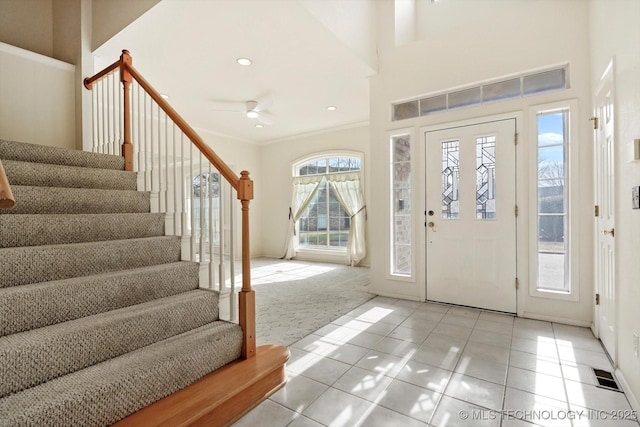 carpeted foyer with ceiling fan and crown molding