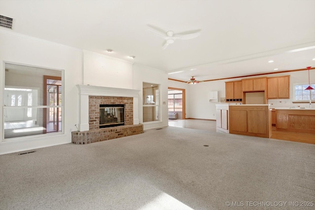 unfurnished living room with ceiling fan, a brick fireplace, crown molding, and light carpet