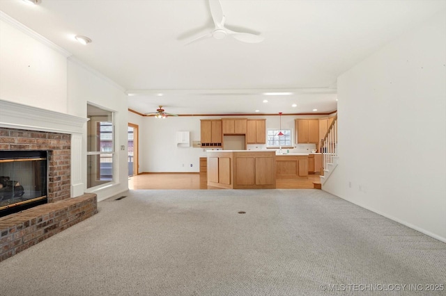 unfurnished living room featuring ceiling fan, light colored carpet, a fireplace, and crown molding