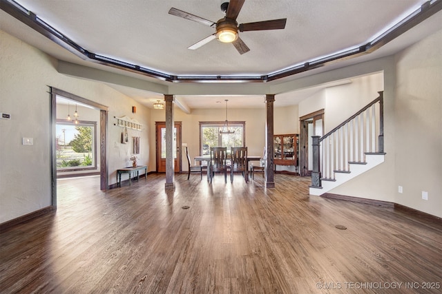 interior space featuring dark hardwood / wood-style flooring, ceiling fan with notable chandelier, a textured ceiling, and ornate columns