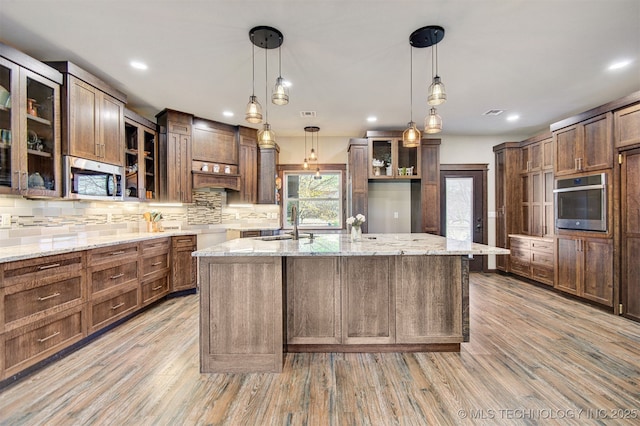 kitchen featuring stainless steel appliances, an island with sink, pendant lighting, and light hardwood / wood-style floors