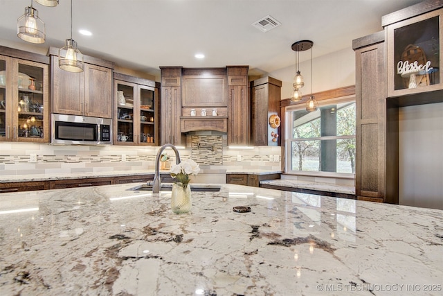 kitchen featuring sink, light stone counters, pendant lighting, and decorative backsplash