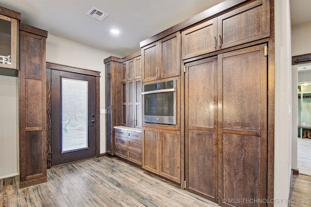 kitchen featuring dark brown cabinets, oven, and light hardwood / wood-style flooring