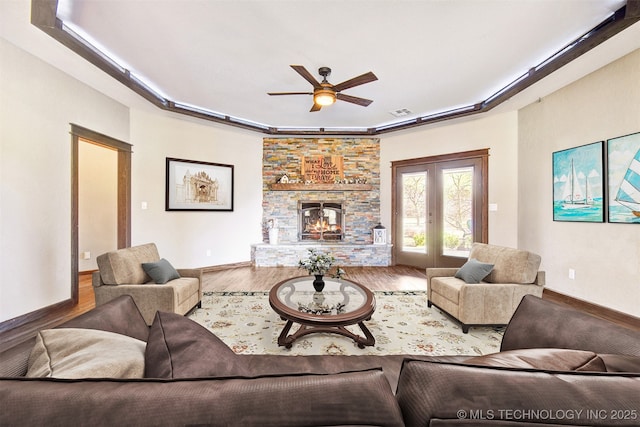 living room with french doors, a stone fireplace, a raised ceiling, ceiling fan, and hardwood / wood-style floors