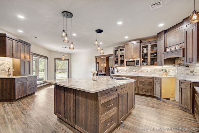 kitchen with sink, light hardwood / wood-style flooring, a large island with sink, pendant lighting, and backsplash