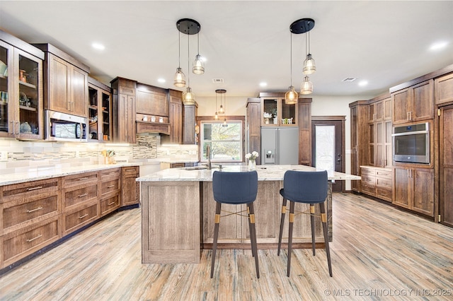 kitchen featuring appliances with stainless steel finishes, a kitchen breakfast bar, hanging light fixtures, a center island with sink, and light hardwood / wood-style flooring