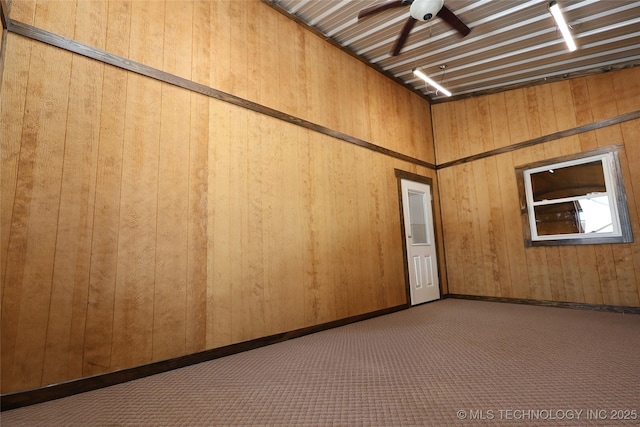 carpeted empty room featuring ceiling fan and wooden walls