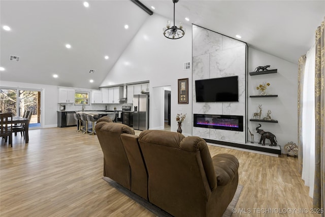 living room featuring high vaulted ceiling, a chandelier, a tile fireplace, and light hardwood / wood-style flooring