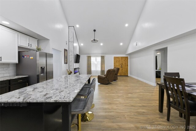 kitchen featuring a center island, white cabinets, stainless steel refrigerator with ice dispenser, and high vaulted ceiling