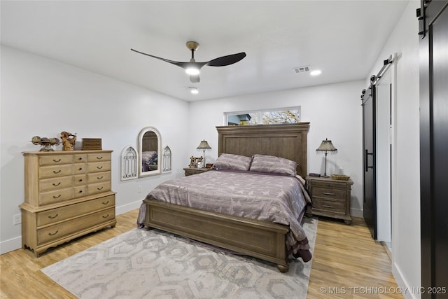 bedroom with light wood-type flooring, a barn door, and ceiling fan