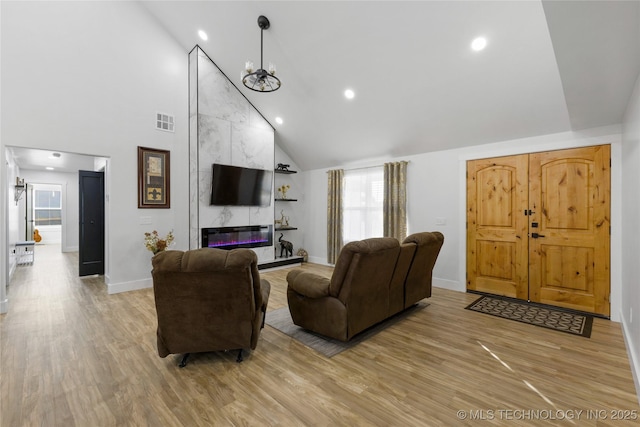 living room with an inviting chandelier, a fireplace, high vaulted ceiling, and light hardwood / wood-style flooring