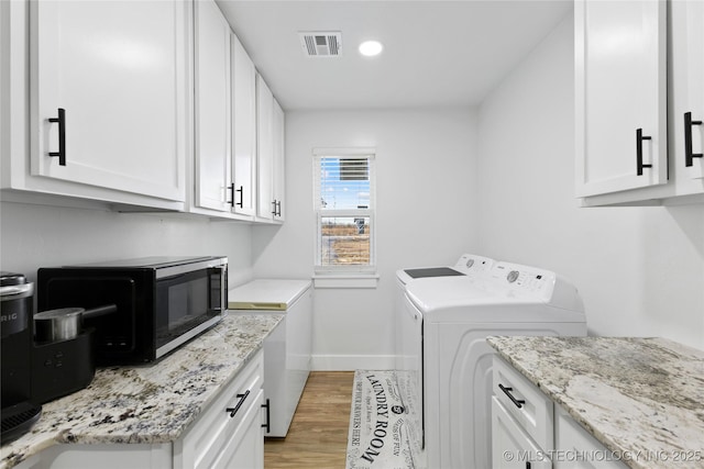 clothes washing area featuring cabinets, light hardwood / wood-style flooring, and washing machine and clothes dryer