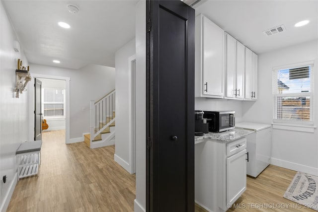 kitchen with white cabinetry, light stone counters, and light wood-type flooring