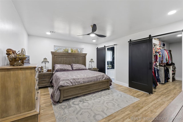 bedroom with light wood-type flooring, a barn door, a closet, and ceiling fan