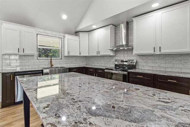 kitchen featuring sink, vaulted ceiling, wall chimney exhaust hood, white cabinetry, and stainless steel appliances