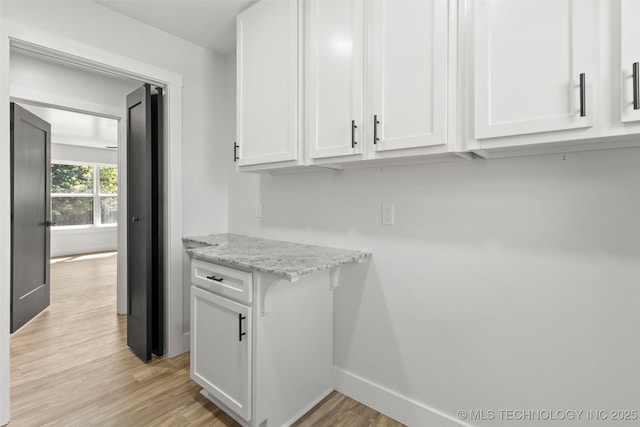 kitchen featuring white cabinets, light wood-type flooring, and light stone counters