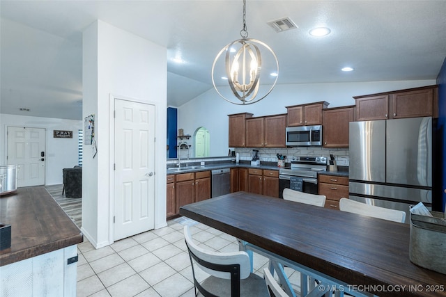 kitchen with decorative backsplash, stainless steel appliances, an inviting chandelier, lofted ceiling, and light tile patterned flooring