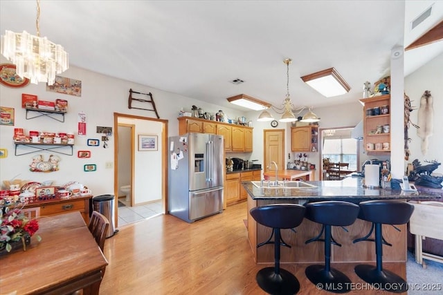 kitchen with kitchen peninsula, stainless steel fridge with ice dispenser, a notable chandelier, and sink