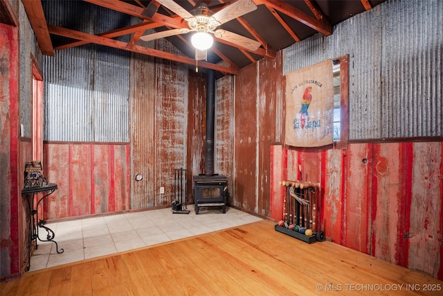 unfurnished living room featuring vaulted ceiling with beams, hardwood / wood-style flooring, ceiling fan, and a wood stove