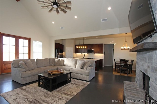 living room featuring ceiling fan with notable chandelier, a stone fireplace, sink, and high vaulted ceiling