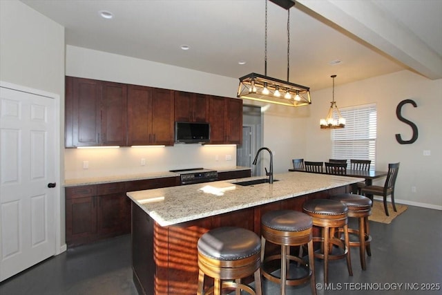 kitchen featuring pendant lighting, black appliances, a kitchen breakfast bar, sink, and an island with sink