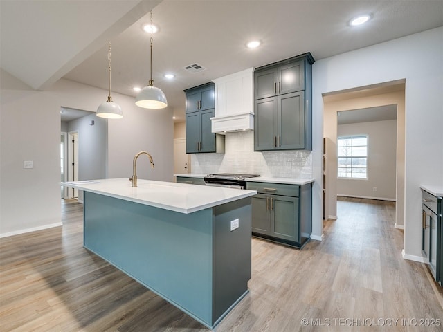 kitchen with an island with sink, sink, decorative backsplash, hanging light fixtures, and stainless steel range oven