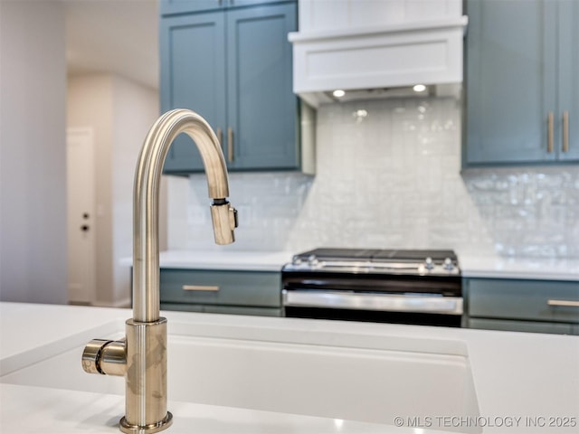 kitchen with tasteful backsplash, blue cabinetry, stainless steel range oven, and sink