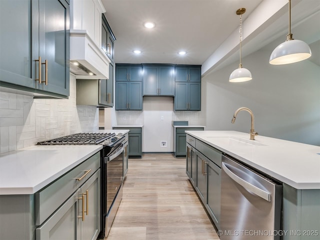 kitchen featuring decorative light fixtures, sink, stainless steel dishwasher, a center island with sink, and gas range oven