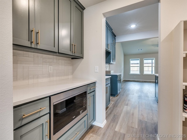 kitchen featuring tasteful backsplash, light hardwood / wood-style flooring, gray cabinetry, and black microwave