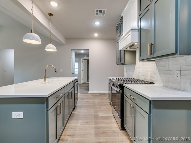 kitchen with hanging light fixtures, backsplash, stainless steel appliances, light hardwood / wood-style floors, and an island with sink