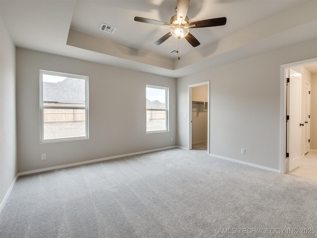 empty room featuring light carpet, a tray ceiling, and ceiling fan