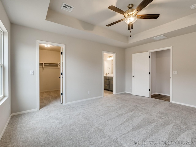 unfurnished bedroom featuring a tray ceiling, light colored carpet, ceiling fan, and a spacious closet