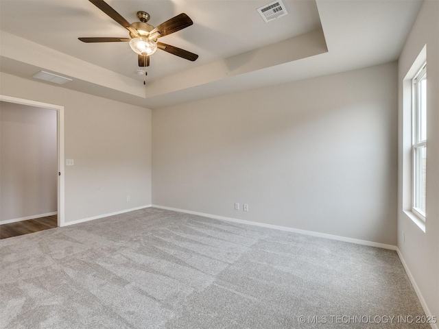 carpeted spare room featuring ceiling fan, a raised ceiling, and a healthy amount of sunlight