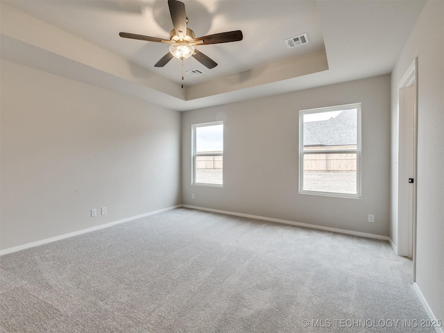 empty room featuring a raised ceiling, light carpet, and ceiling fan