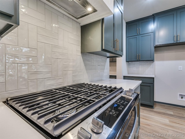 kitchen featuring premium range hood, backsplash, gas range, blue cabinetry, and light wood-type flooring