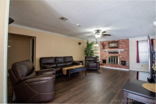 living room with a brick fireplace, ornamental molding, a textured ceiling, ceiling fan, and dark wood-type flooring