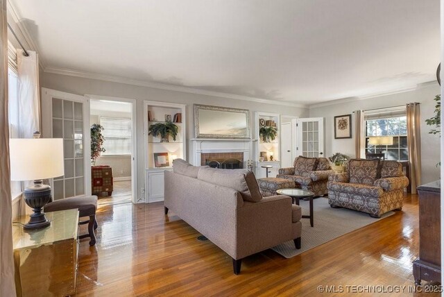 living room with french doors, wood-type flooring, ornamental molding, and a brick fireplace