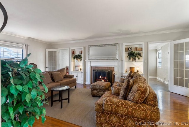 living room featuring a tiled fireplace, crown molding, a healthy amount of sunlight, and hardwood / wood-style flooring