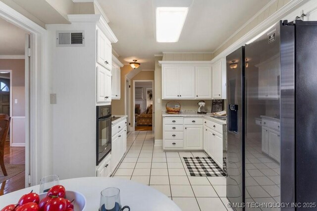 kitchen with stainless steel fridge, white cabinets, oven, and light tile patterned floors