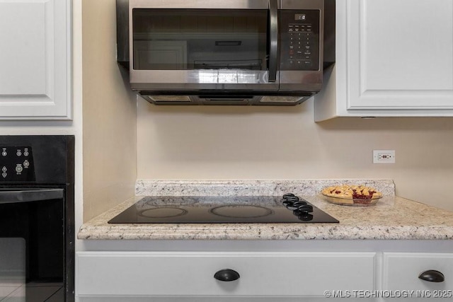 kitchen featuring black appliances, white cabinets, and light stone counters