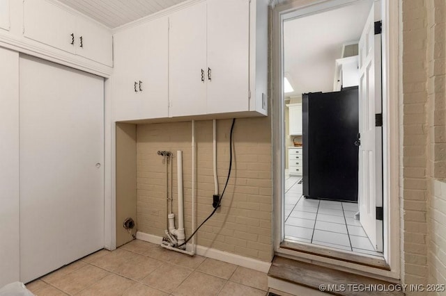 laundry area with light tile patterned flooring, crown molding, and brick wall