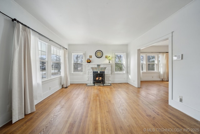 unfurnished living room with a stone fireplace, wood-type flooring, and a wealth of natural light