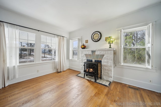 living room with hardwood / wood-style floors, a wood stove, a healthy amount of sunlight, and crown molding