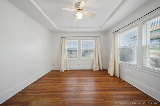 empty room with a tray ceiling, ceiling fan, a healthy amount of sunlight, and dark hardwood / wood-style floors