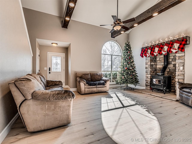 living room featuring beam ceiling, light wood-type flooring, a wood stove, and ceiling fan