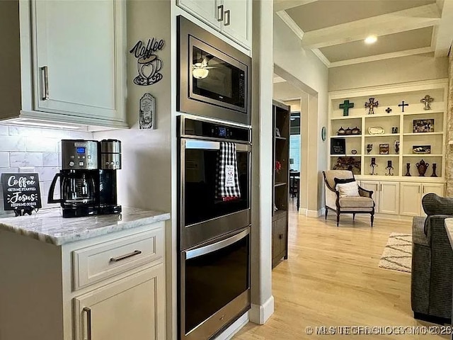 kitchen with white cabinets, light wood-type flooring, tasteful backsplash, light stone counters, and stainless steel appliances