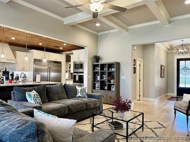 living room featuring ceiling fan with notable chandelier, crown molding, sink, beam ceiling, and light hardwood / wood-style flooring