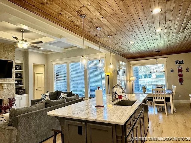 kitchen with light stone counters, ceiling fan, sink, decorative light fixtures, and a fireplace